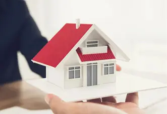 A person holding a small model house in their hand.