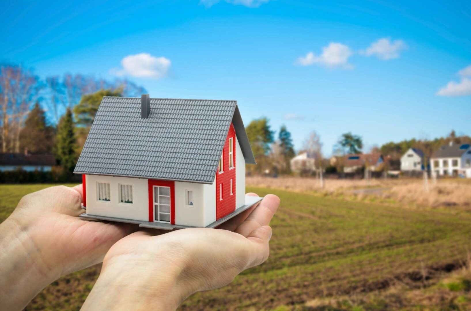 A person holding a small model house in their hand.