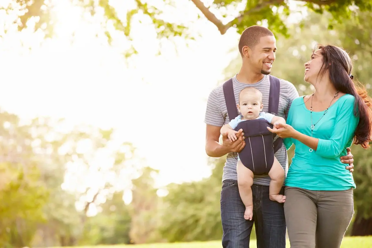 A man and woman holding a baby in a carrier.